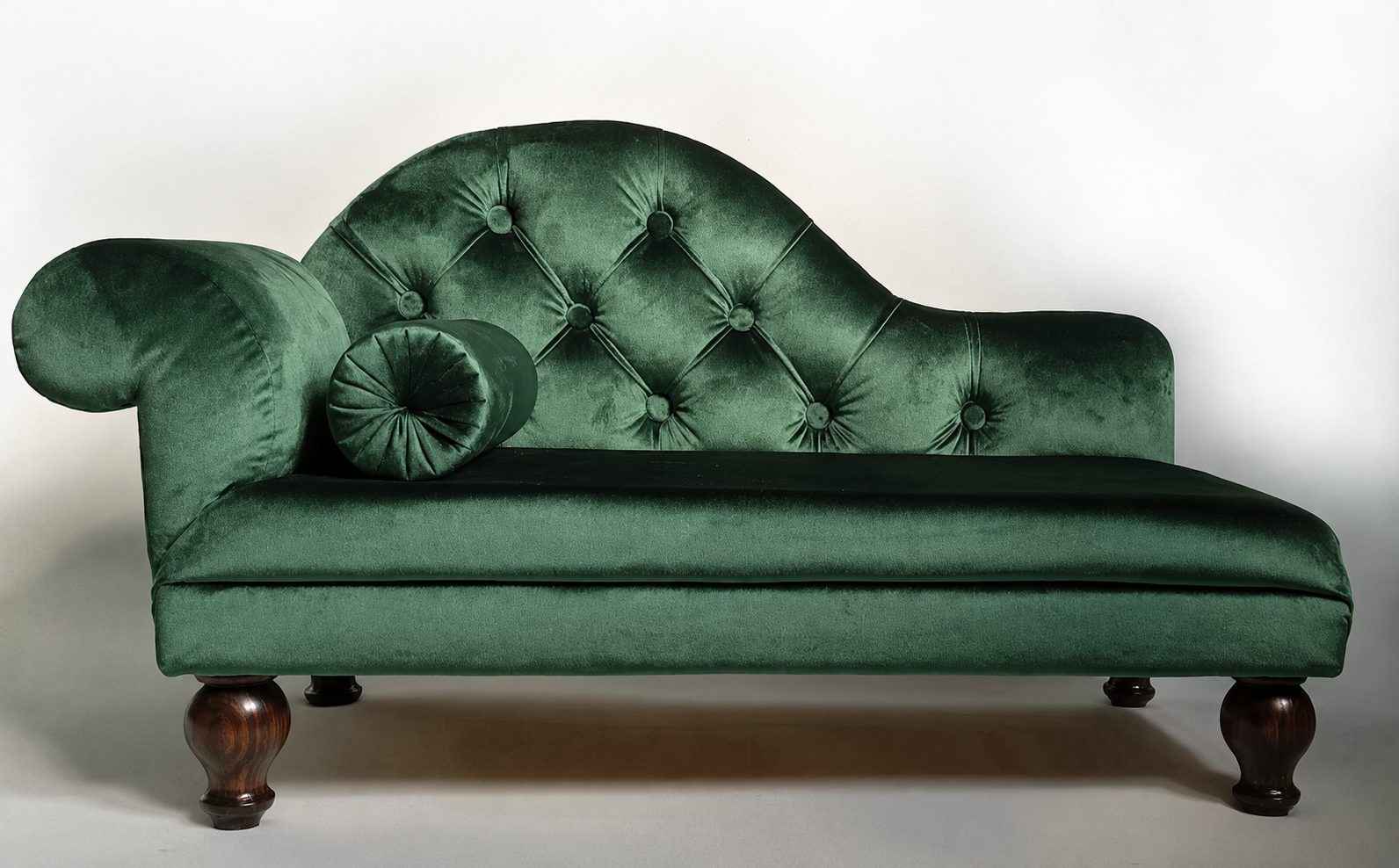 Green velvet chaise lounge with tufted backrest on a white background